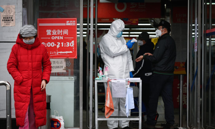 Un employé d'un supermarché portant une combinaison de protection utilise un thermomètre pour vérifier la température d'un arrivant à l'entrée d'un supermarché à Pékin le 29 février 2020. - Le 29 février, la Chine a fait état de 47 décès supplémentaires dus au nouveau coronavirus, ce qui porte le nombre de décès dans le pays à 2 835. (Photo par STR / AFP) (Photo par STR/AFP via Getty Images)