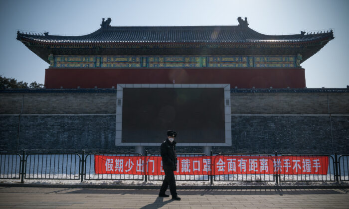 Un agent de sécurité passe devant une bannière de propagande disant "Ne quittez pas souvent la maison pendant les vacances, portez un masque lorsque vous sortez, gardez une distance et ne serrez pas la main lorsque vous vous rencontrez" dans le parc du Temple du Ciel, à Pékin, en Chine, le 15 février 2020. (Andrea Verdelli/Getty Images)