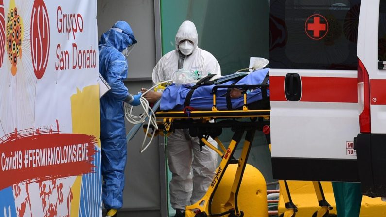 Le 23 mars 2020, des travailleurs médicaux font passer un patient d'une ambulance de la Croix-Rouge italienne à une unité de soins intensifs installée dans un centre sportif devant l'hôpital San Raffaele de Milan. (Miguel Medina/AFP via Getty Images)