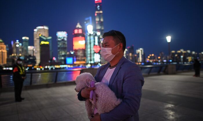 Un homme porte un masque facial, préoccupé par l'épidémie du virus du PCC, se promène avec son chien sur la promenade du Bund le long de la rivière Huangpu à Shanghai, en Chine, le 20 mars 2020. (Hector Retamal/AFP via Getty Images)