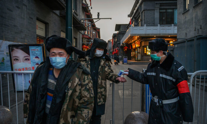 Un Chinois porte un masque de protection alors que lui et d'autres personnes font vérifier leur température par un garde à l'entrée temporaire d'une zone commerciale à Pékin, le 11 mars 2020. (Kevin Frayer/Getty Images)