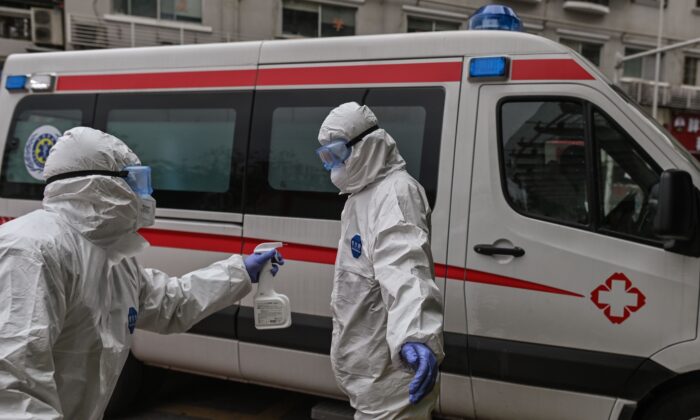 Le 30 mars 2020, à l'hôpital de la Croix-Rouge de Wuhan, en Chine, un ambulancier pulvérise du désinfectant sur son collègue après avoir transporté un patient récemment guéri du virus du PCC. (HECTOR RETAMAL/AFP via Getty Images)