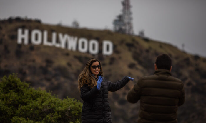 Une femme portant des gants hygiéniques pose sous le signe d'Hollywood à Hollywood, en Californie, le 22 mars 2020. (Apu Gomes/AFP via Getty Images)