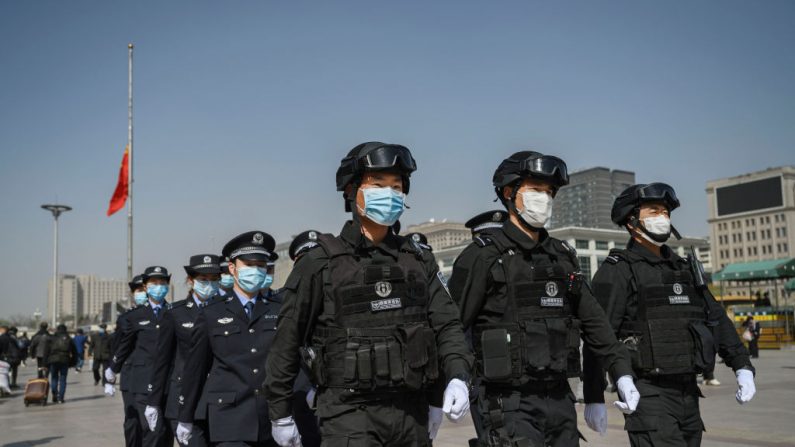 Des policiers chinois portent des masques de protection alors qu'ils marchent en formation en s'éloignant d'un drapeau national en berne après avoir observé trois minutes de silence pour marquer le jour de deuil national du pays pour le COVID-19 à la gare ferroviaire de Pékin, le 4 avril 2020. (Kevin Frayer/Getty Images)