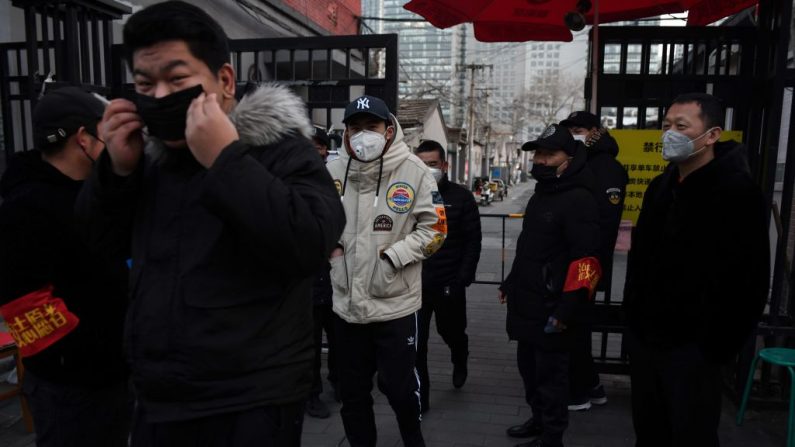 Des habitants portent des masques de protection alors qu'ils passent devant les bénévoles qui tiennent un poste de contrôle à l'entrée d'une ruelle de Pékin, le 21 février 2020. (Greg Baker/AFP via Getty Images)