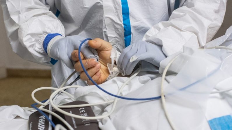 Un membre du personnel soignant dans une combinaison de protection tient la main d'un patient atteint du virus du PCC alors qu'il est transféré à un autre étage des soins intensifs de l'hôpital universitaire de Bellvitge à L'Hospitalet del Llobregat, près de Barcelone, en Espagne, le 9 avril 2020 (David Ramos / Getty Images)