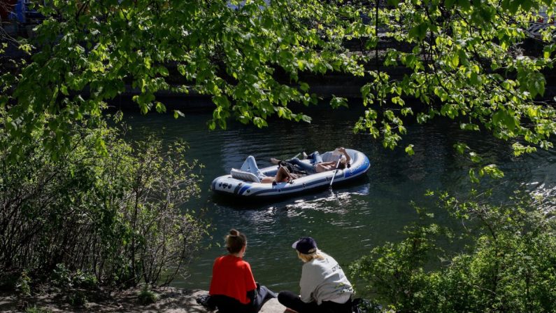 Le 18 avril 2020, des personnes s'assoient au soleil tandis que d'autres se détendent sur un bateau gonflable le long du canal de la Landwehr, dans le quartier de Kreuzberg à Berlin. (David Gannon/AFP via Getty Images)