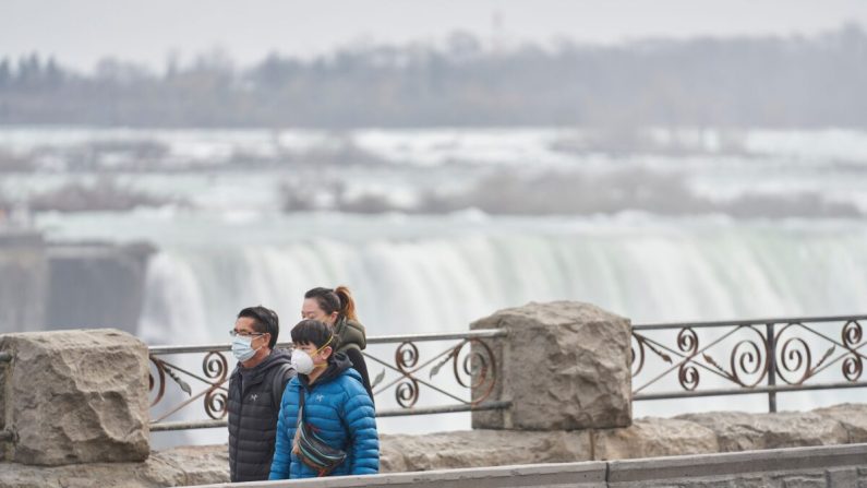Des touristes portant des masques traversent à pied le Fer à cheval (Horseshoe Falls, ou chutes canadiennes), aux chutes du Niagara, Ontario, Canada, le 18 mars 2020. (Geoff Robins/AFP via Getty Images)
