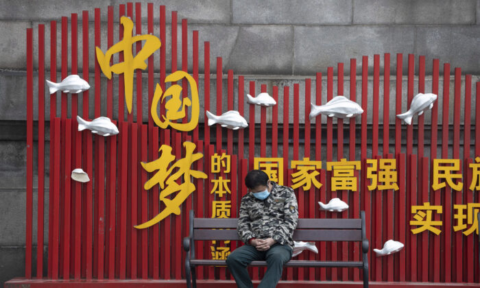 Un habitant portant un masque fait la sieste sur un banc près du slogan de propagande du gouvernement "Le rêve chinois" à Wuhan, en Chine, le 1er avril 2020. (AP Photo/Ng Han Guan)