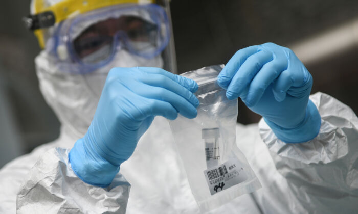 Un membre du personnel médical prélève un échantillon dans un collège alors que les élèves subissent un test d'acide nucléique pour le virus du PCC à Guangzhou, en Chine, le 21 avril 2020. (STR/AFP via Getty Images)