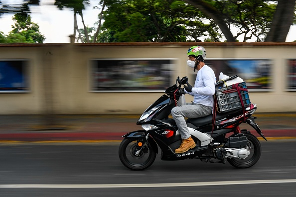 -Un volontaire conduit une moto transportant des repas à livrer aux personnes âgées dans le cadre du "Bon voisinage", à Caracas, le 28 avril 2020. Photo de FEDERICO PARRA / AFP via Getty Images.