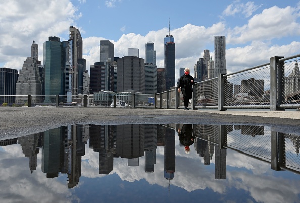 -Une femme portant un masque facial et l'horizon du bas de Manhattan se reflètent dans une flaque d'eau après de fortes pluies le 11 mai 2020 dans le quartier de Brooklyn à New York. Photo par Angela Weiss / AFP via Getty Images.