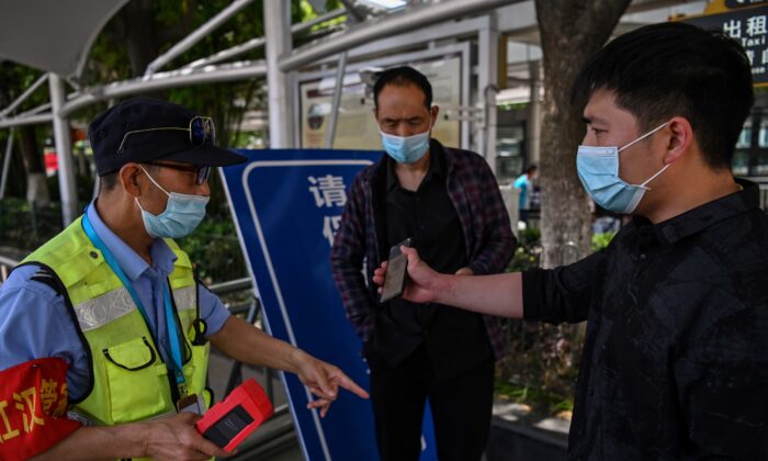 Un travailleur scanne le code de santé généré par l'application du téléphone portable d'un passager et contrôle sa température corporelle avant que le passager ne puisse prendre un taxi à la gare de Hankou à Wuhan, en Chine, le 12 mai 2020. (HECTOR RETAMAL/AFP via Getty Images)