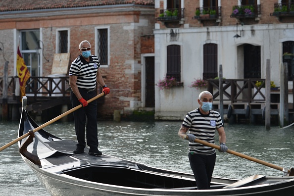 -Les gondoliers portant un masque facial montent en gondole près du quai de San Toma sur un canal de Venise alors qu'ils reprennent le service le 18 mai 2020. Photo par ANDREA PATTARO / AFP via Getty Images.