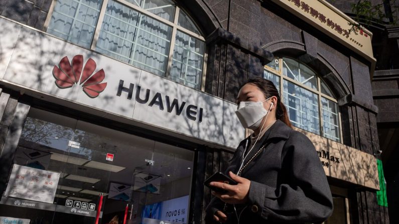 Une femme, portant un masque facial pour contrer l'épidémie de Covid-19, passe devant un magasin Huawei (à gauche) dans une rue de Pékin le 22 avril 2020 en tenant son smartphone. (NICOLAS ASFOURI/AFP via Getty Images)