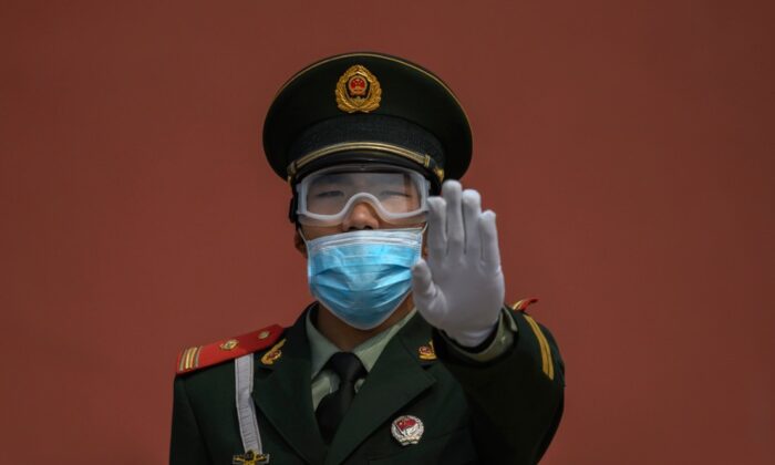 Un officier de police paramilitaire chinois fait un geste alors qu'il porte un masque de protection et monte la garde à l'entrée de la Cité interdite, lors de sa réouverture à un nombre limité de visiteurs à Pékin, en Chine, le 1er mai 2020. (Kevin Frayer/Getty Images)