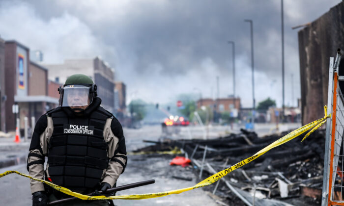 Un policier vu au milieu de la fumée et des débris au lendemain d'une nuit de protestations et de violence à Minneapolis à la suite de la mort de George Floyd, le 29 mai 2020. (Charlotte Cuthbertson/Epoch Times)