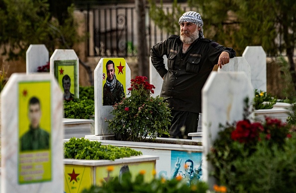 -Un homme se tient près des tombes des combattants kurdes tués avec les Forces démocratiques syriennes. Photo par Delil SOULEIMAN / AFP via Getty Images.