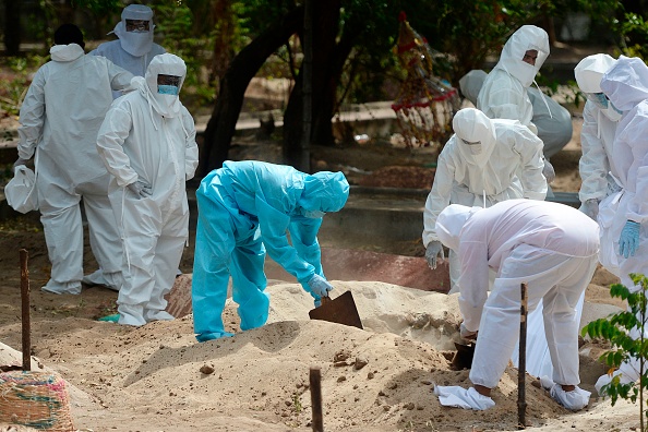 -Des volontaires en Inde portent un équipement de protection, couvrent de sable une victime décédée du coronavirus Covid-19, lors d'une inhumation dans un cimetière de Chennai le 16 juin 2020. (Photo d'Arun SANKAR / AFP via Getty Images)