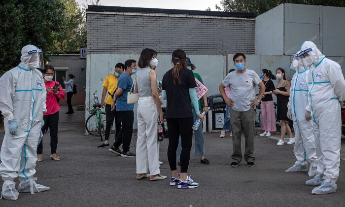 Des travailleurs portant des équipements de protection individuelle s'occupent d'un groupe de personnes portant des masques faciaux en attendant de passer les testspour le  Covid-19 à Pékin le 19 juin 2020. (NICOLAS ASFOURI/AFP via Getty Images)