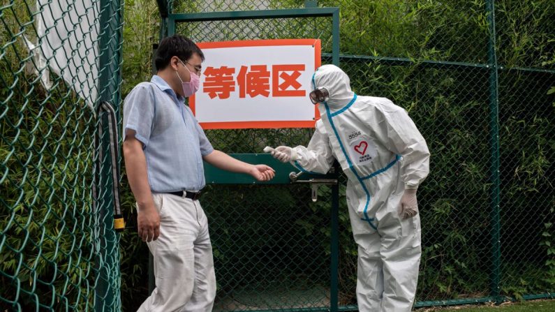 Un homme qui porte un masque facial fait contrôler sa température par un professionnel de la santé muni d'un équipement de protection individuelle alors qu'il entre dans une zone extérieure lors d'un test de masse pour le coronavirus Covid-19 sur le site de test du parc forestier urbain de Xinjiekou, à Pékin, le 24 juin 2020. (Nicolas Asfouri/AFP via Getty Images)