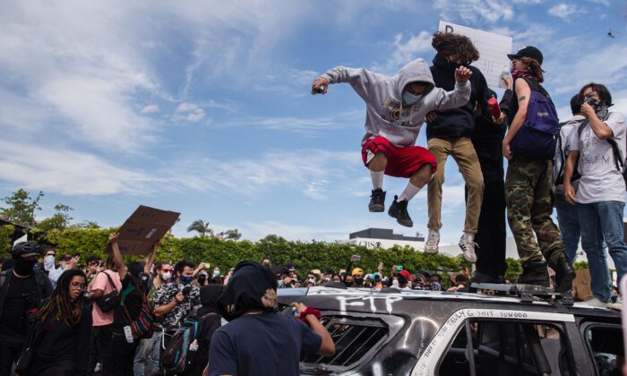 Des manifestants sautant sur un véhicule de police endommagé à Los Angeles le 30 mai 2020, lors d'une manifestation contre la mort de George Floyd. (Ariana Drehsler/AFP via Getty Images)