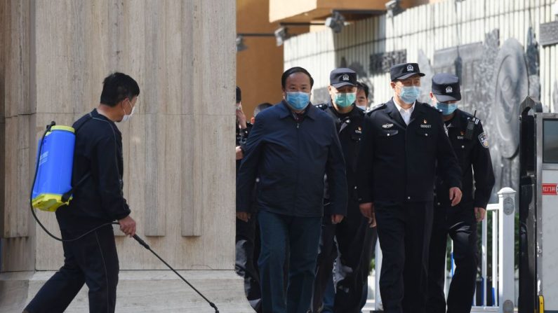 La police et des fonctionnaires sortent d'un lycée alors qu'un homme (à gauche) désinfecte l'entrée du lycée, à Pékin, le 27 avril 2020. (Greg Baker/AFP via Getty Images)