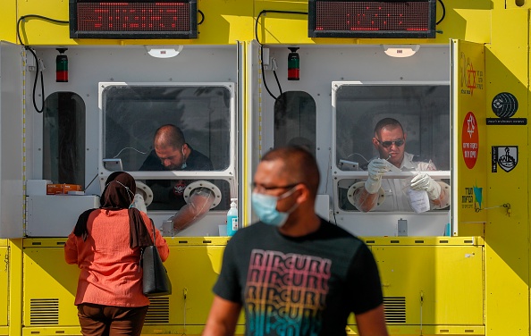 Des ambulanciers paramédicaux d’urgence nationale d'Israël, collectent des échantillons de coton-tige sur une personne dans une station de test mobile pour le coronavirus, à Jérusalem-Est, le 5 juillet 2020. Photo AHMAD GHARABLI / AFP via Getty Images.