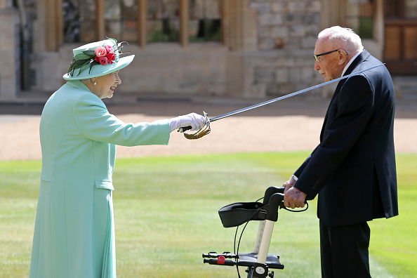 -La reine Elizabeth II de Grande-Bretagne utilise l'épée qui appartenait à son père, George VI, alors qu'elle confère l'honneur de la chevalerie au capitaine Tom Moore, vétéran de la Seconde Guerre mondiale, âgé de 100 ans, au château de Windsor à Windsor, à l'ouest de Londres, le 17 juillet 2020. Photo de CHRIS JACKSON / POOL / AFP via Getty Images.