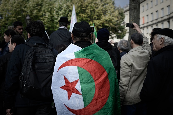 Ceint du drapeau de l’Algérie, un homme participe à un rassemblement organisé près de l’Assemblée nationale à Paris le 24 octobre 2019 pour dénoncer la répression des manifestants du « Hirak » en Algérie. PHILIPPE LOPEZ/AFP via Getty Images.