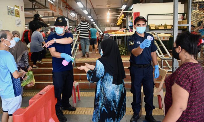Le personnel de sécurité vérifie la température des personnes qui entrent dans un marché, tout en appliquant la distanciation sociale, à Penang, en Malaisie, le 29 mai 2020. (Goh Chai Hin/AFP via Getty Images)