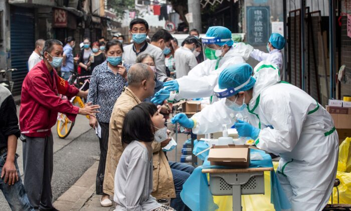  Le 15 mai 2020, dans une rue de Wuhan, dans la province centrale du Hubei en Chine, des travailleurs médicaux prélèvent des échantillons par écouvillonnage sur des résidents pour les soumettre à un test de dépistage du coronavirus COVID-19 (STR/AFP via Getty Images)