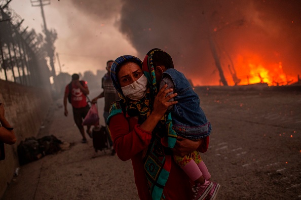 Une femme porte un enfant devant les flammes après qu'un incendie majeur se soit déclaré dans le camp de migrants de Moria sur l'île grecque égéenne de Lesbos, le 9 septembre 2020.(Photo : ANGELOS TZORTZINIS/AFP via Getty Images)