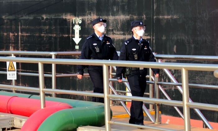 Des policiers masqués regardent un pétrolier décharger du pétrole brut dans le port de Qingdao, dans la province du Shandong, à l'est de la Chine, le 20 mars 2020. (STR/AFP via Getty Images)