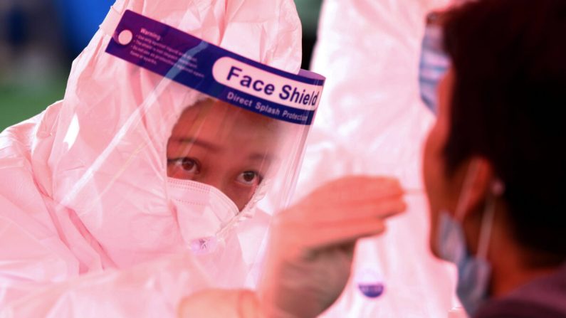 Un professionnel de la santé (à gauche) prélève un échantillon sur un habitant pour le soumettre au test de dépistage du Covid-19 effectué lors d'un programme de dépistage de masse organisé à la suite d'une nouvelle vague de l'épidémie à Qingdao, dans la province du Shandong, à l'Est de la Chine, le 14 octobre 2020. (STR/AFP via Getty Images)