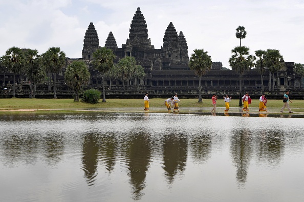 -Des touristes passent devant le temple d'Angkor Wat au Cambodge. Une équipe de jardiniers escalade avec précaution l'extérieur du temple pour couper le feuillage avant qu'il n'endommage l'ancienne façade. Photo Tang Chhin Sothy / AFP via Getty Images.