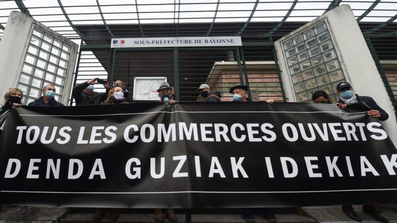 Des commerçants brandissent une banderole portant l'inscription « Tous les magasins sont ouverts » lors d'une manifestation devant la sous-préfecture pour exiger la réouverture de petits commerces « non essentiels », à Bayonne, dans le sud-ouest de la France, le 4 novembre 2020. (GAIZKA IROZ/AFP via Getty Images)