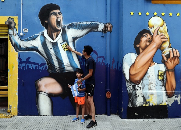 -Un homme et son enfant rendent hommage à côté d'une peinture murale représentant la légende du football argentin Diego Maradona dans le quartier de La Boca, à Buenos Aires, le 25 novembre 2020, le jour de sa mort. Photo par Alejandro Pagni / AFP via Getty Images.