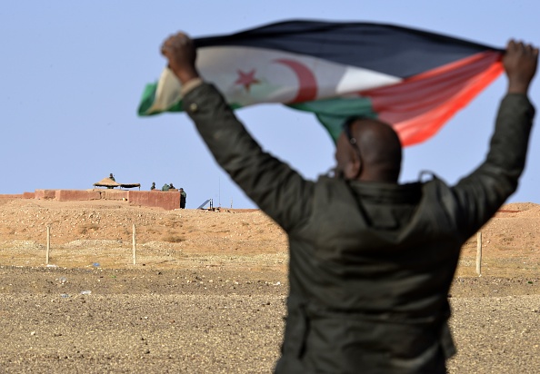 -Un homme sahraoui brandit un drapeau du Front Polisario dans la zone d'Al-Mahbes près des soldats marocains gardant le mur séparant le Sahara Occidental. photo Stringer / AFP via Getty Images.