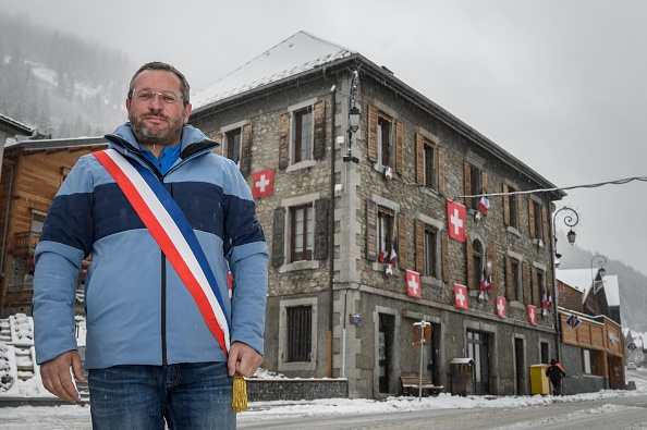 Le maire de Châtel, Nicolas Rubin, devant la mairie de sa commune de Haute-Savoie sur laquelle il a accroché des drapeaux suisses pour protester contre les décisions gouvernementales concernant les stations de ski. (FABRICE COFFRINI/AFP via Getty Images)