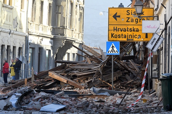 Les gens se tiennent à côté des décombres des bâtiments endommagés à Petrinja, à environ 50 km de Zagreb, après que la ville a été frappée par un tremblement de terre de magnitude 6,4 le 29 décembre 2020.  (Photo : DENIS LOVROVIC/AFP via Getty Images)