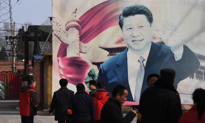 Des gens se tiennent près d'un panneau de propagande décoloré sur lequel figure l'image du leader chinois Xi Jinping, dans un stationnement de Pékin, le 19 mars 2018. (Greg Baker/AFP via Getty Images)