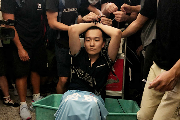 -Un homme soupçonné d'être un espion chinois est ligoté par des manifestants à l'aéroport international de Hong Kong lors d'une manifestation le 13 août 2019 à Hong Kong. Photo par Anthony Kwan / Getty Images.