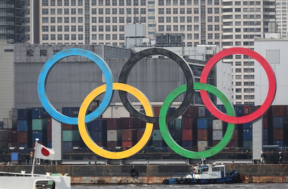 -Un drapeau japonais flotte près d'un symbole d'anneaux olympiques de grande taille. Photo par Behrouz Merhi / AFP via Getty Images.
