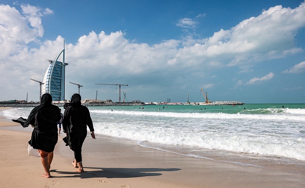 -Des femmes marchent le long du rivage alors que les surfeurs prennent les vagues, à Dubaï le 24 novembre 2020. Photo par Giuseppe Cacace / AFP via Getty Images.