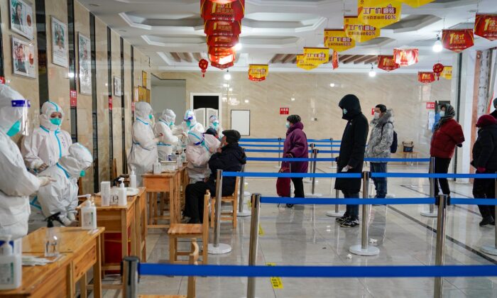 Le 14 janvier 2021, un soignant prélève un échantillon sur un homme alors que des personnes font la queue pour obtenir des tests de dépistage du coronavirus Covid-19 dans un immeuble de bureaux à Harbin, dans la province de Heilongjiang au nord-est de la Chine, après que la province a déclaré l' « état d'urgence » alors que le nombre de cas quotidiens de Covid-19 augmente. (STR/AFP via Getty Images)
