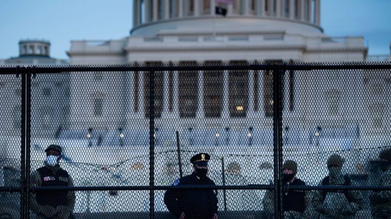 Un officier de la police du Capitole se tient avec des membres de la Garde nationale derrière une clôture de contrôle entourant le Capitole, le lendemain de l'infraction du groupe qui a pénétré dans le Capitole américain à Washington, le 7 janvier 2021. (Brendan Smialowski/AFP via Getty Images)