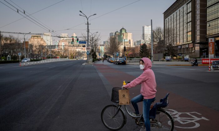 Une femme portant un masque est assise sur son vélo à un feu rouge dans une rue presque vide de Pékin, le 22 mars 2020. (Nicolas Asfouri/AFP via Getty Images)