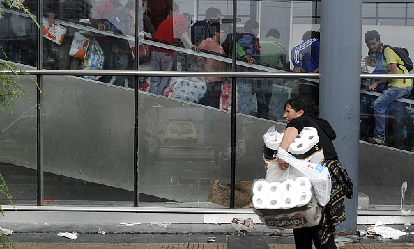 -Une femme porte des sacs de papier toilette et des gens sont vus en arrière-plan en train de piller un supermarché. Photo Daniel Garcia / AFP via Getty Images.