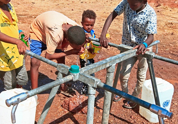 -Un enfant boit l'eau du robinet d’une citerne dans un camp de réfugié. Photo par Ebrahim Hamid / AFP via Getty Images.